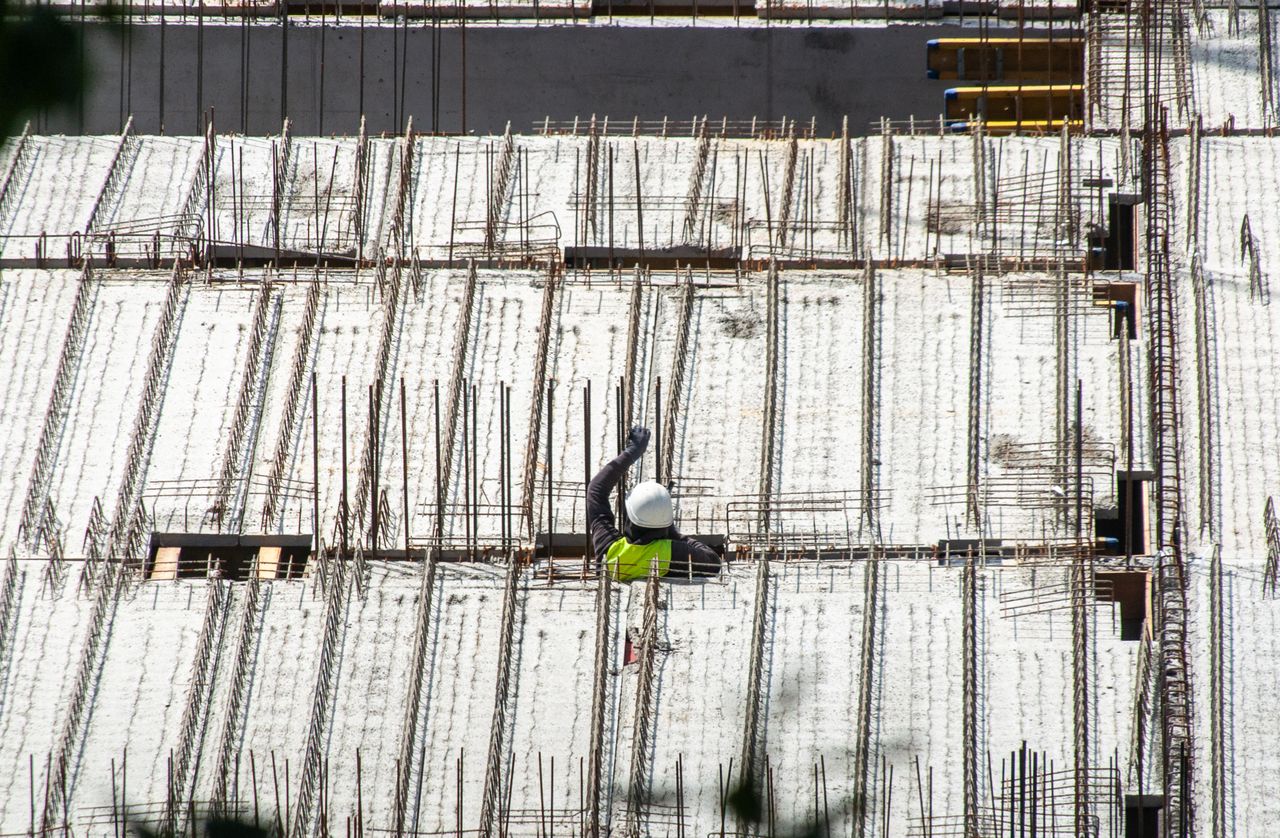 About Aerial view of a construction worker on a building site, showcasing a structural framework with rebar.